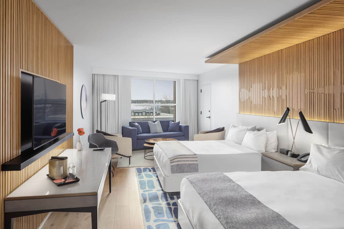 A modern hotel room with a large bed, a sofa, a TV, and a desk with a lamp.