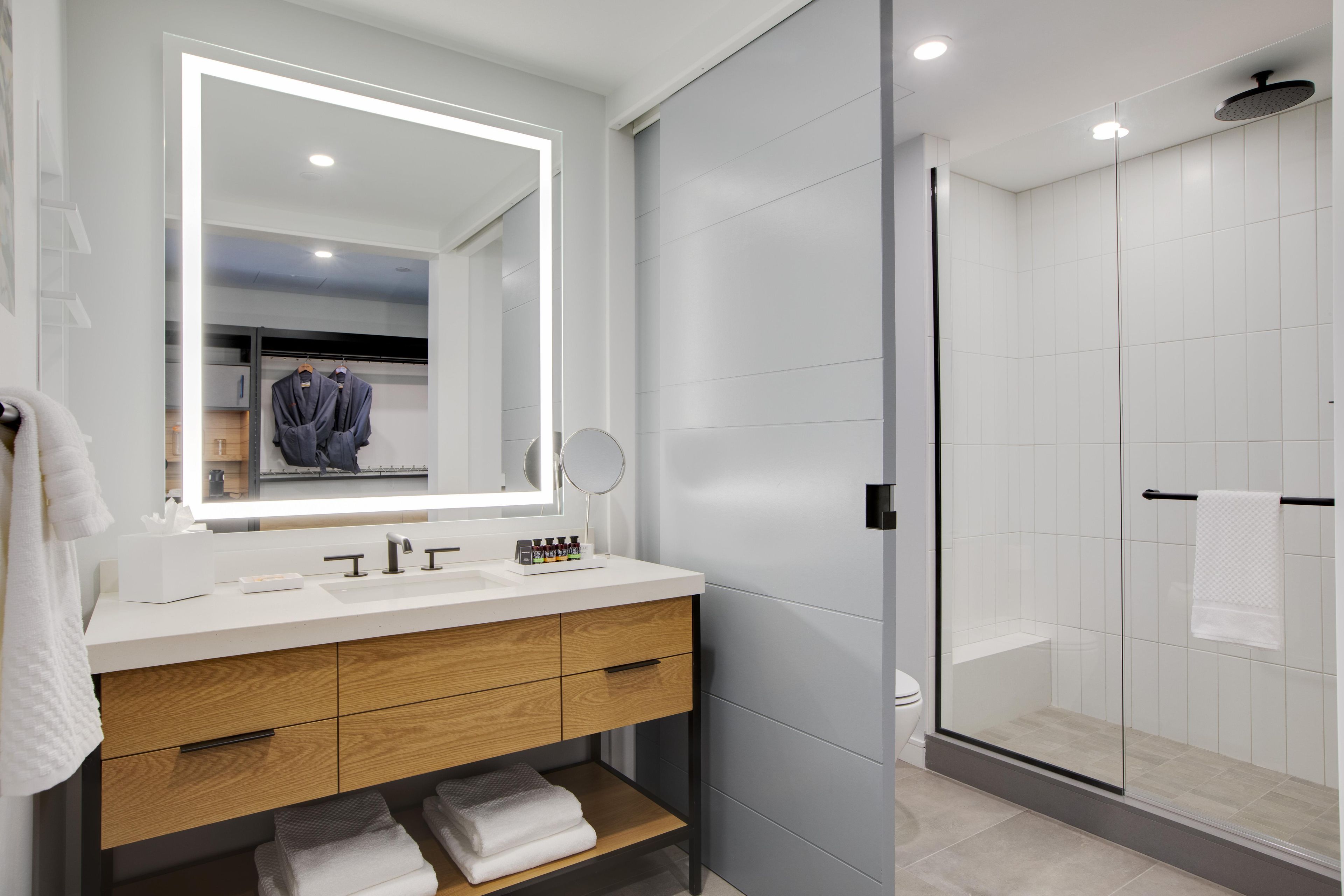 A modern bathroom with a large mirror, dual sinks, and a glass shower enclosure.