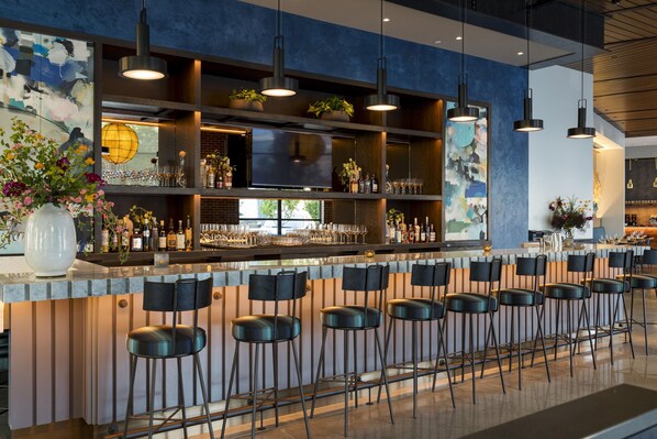 A bar area with a long counter, multiple stools, and a television screen.