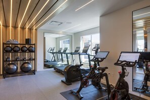 A gym with exercise equipment, treadmills, and a mirrored wall.