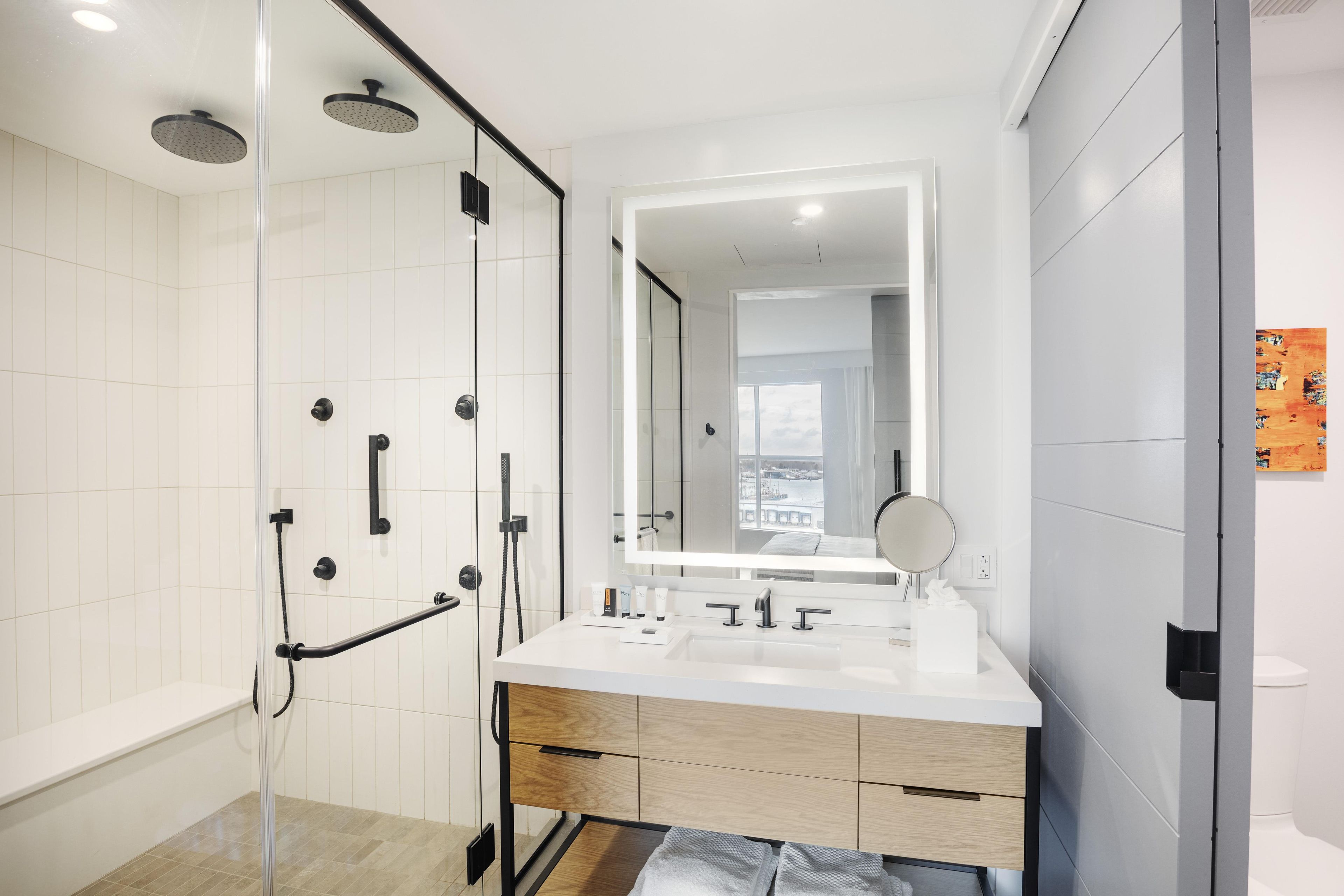 A modern bathroom with a glass shower enclosure, a large mirror, and a white vanity with a sink.