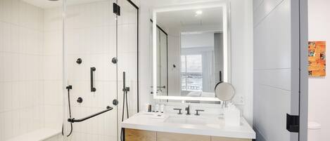 A modern bathroom with a glass shower enclosure, a large mirror, and a white vanity with a sink.