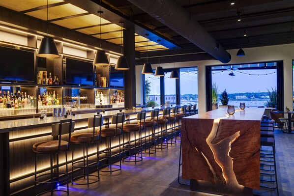 Un bar moderne doté d’un long comptoir, de nombreux tabourets et d’une grande fenêtre donnant sur le paysage urbain.
