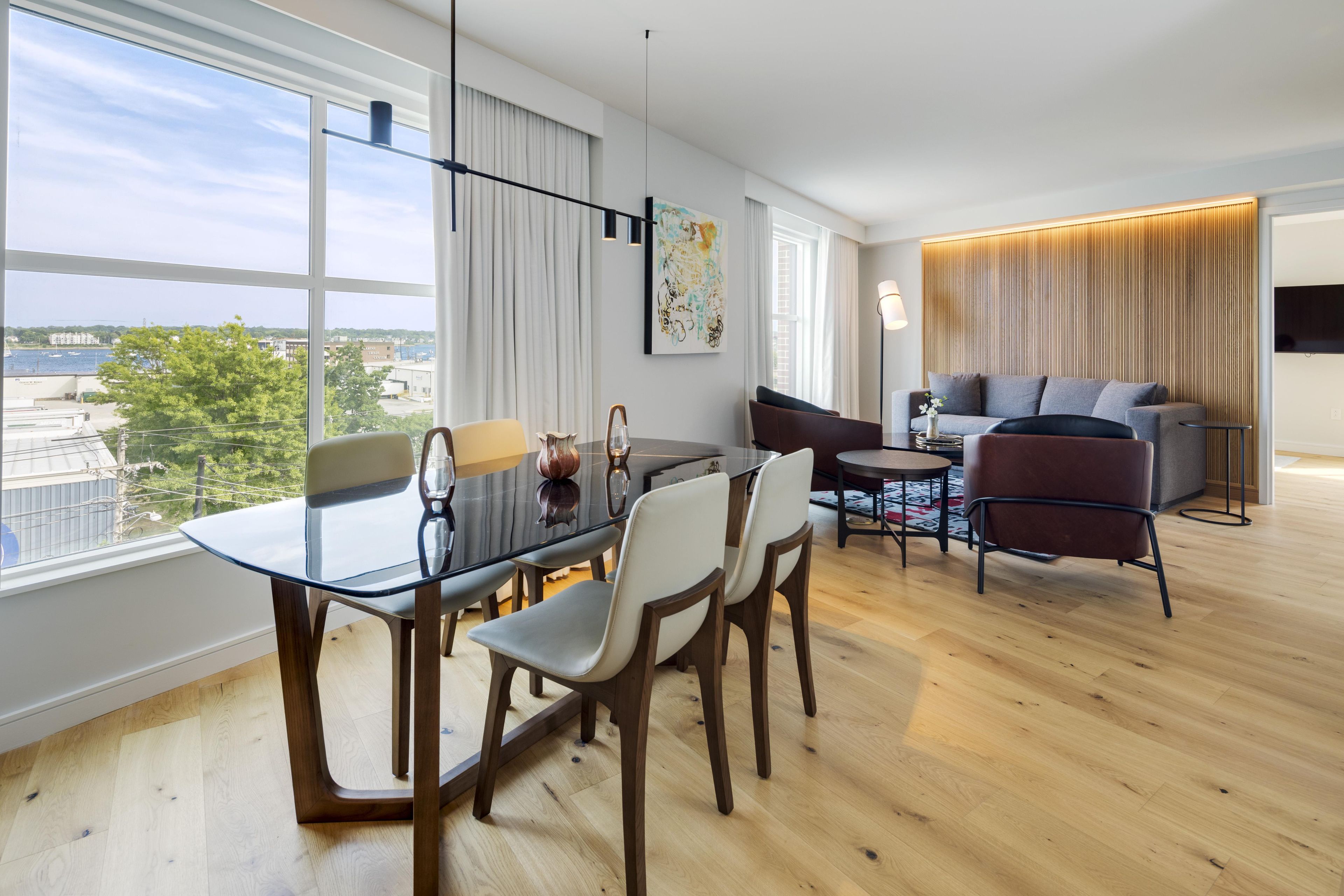 A modern living room with a dining area, large windows, and a view of the city.