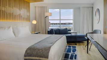 Une chambre d’hôtel équipée d’un lit, d’un bureau, d’une chaise, offrant une vue sur la mer et dotée d’un décor mural moderne.