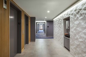 A hotel corridor with wooden paneling on one side, a blue carpet, and a geometric wall design on the other.