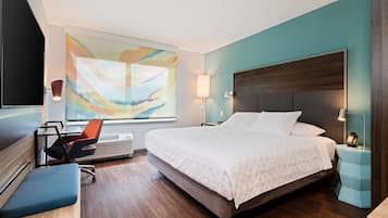 Una habitación de hotel moderna con una cama grande, un escritorio con silla, una lámpara de pie y un cuadro abstracto de gran tamaño en la pared.