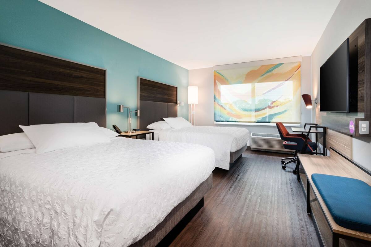 Ein Hotelzimmer mit zwei Betten, einem Schreibtisch, einem Sessel und einem großen abstrakten Gemälde an der Wand.