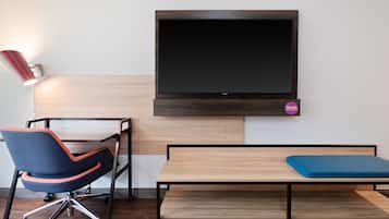 Una habitación moderna con una televisión montada en la pared, un escritorio con una silla y un banco con cojín.