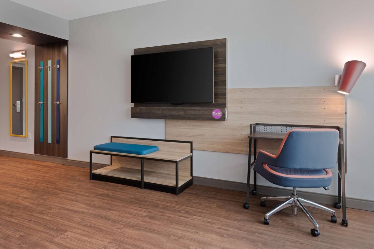 Ein modernes Zimmer mit einem an einer Holzplatte befestigten Flachbildfernseher, einem blauen Bürostuhl und einer kleinen blauen Bank.