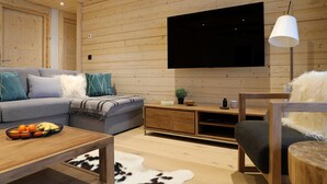 Een gezellige woonkamer met een bank, een bijzettafeltje met fruit, een houten tv-meubel en een wandgemonteerde televisie.