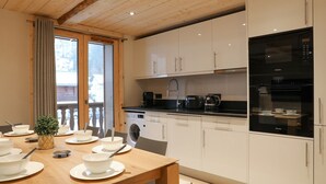 Een moderne keuken met witte kastjes, een houten eettafel gedekt met kommen en borden, een wasmachine en een koffiezetapparaat.