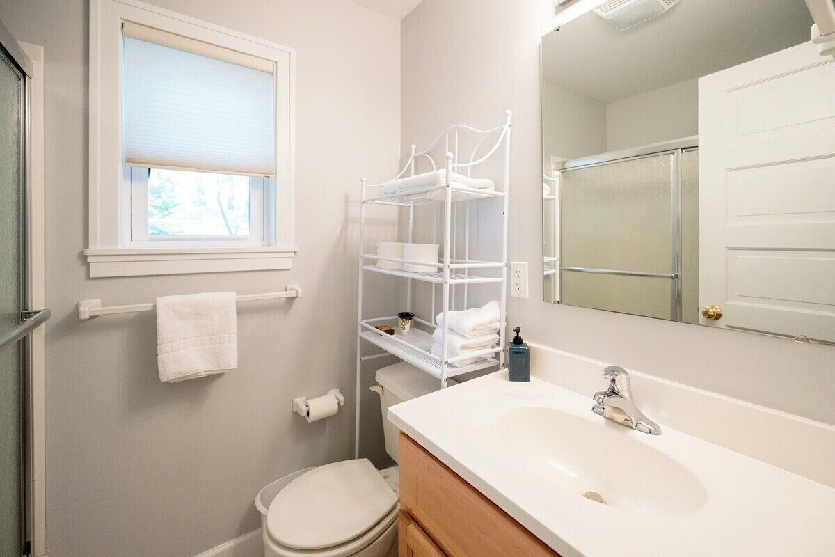 A bathroom with a white sink, a mirror, a toilet, and a window with blinds.