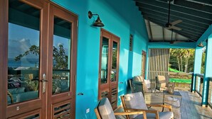 Eine überdachte Veranda mit Holzboden, einer blauen Wand und Blick auf den Ozean.