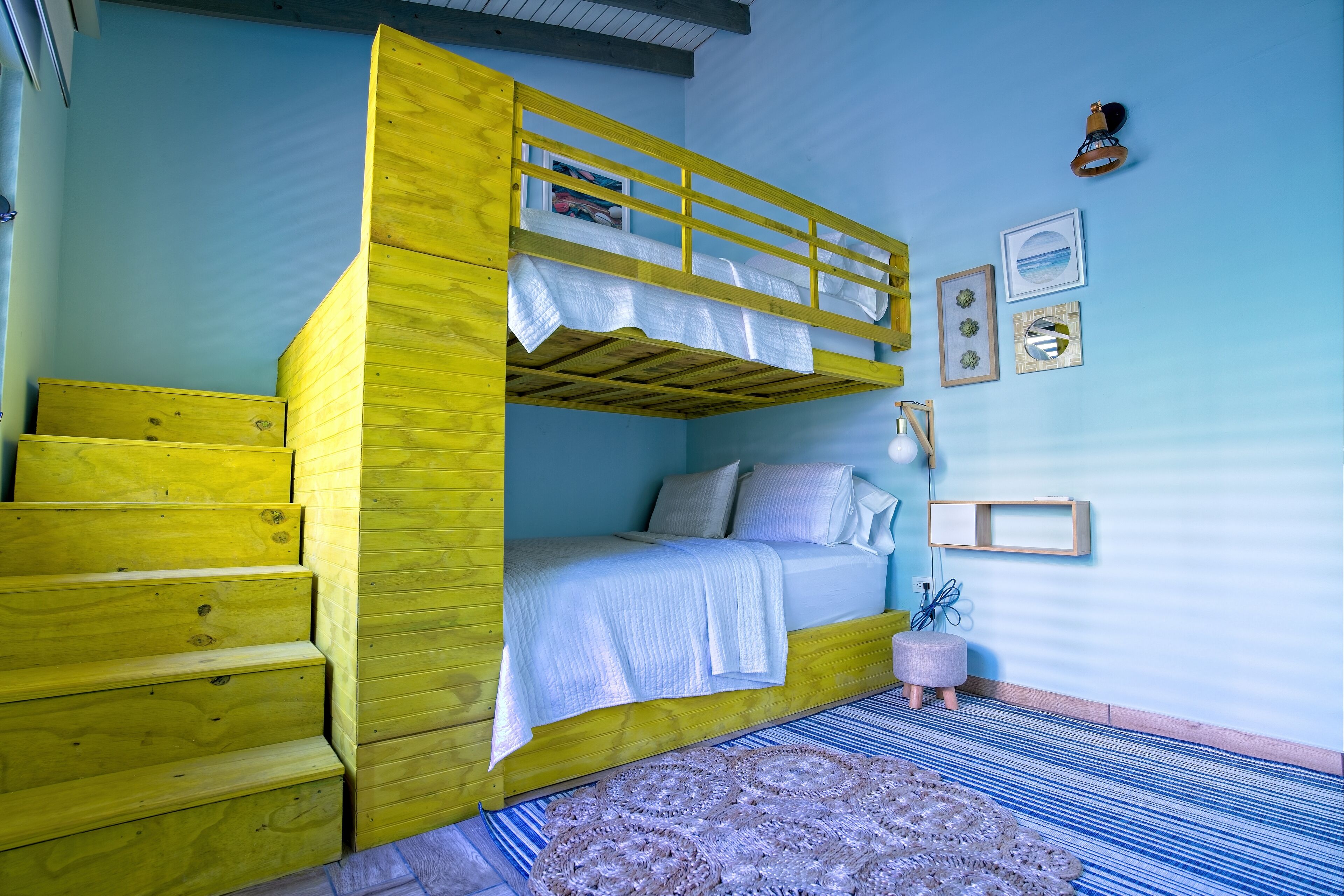 A bunk bed with a wooden ladder, a bedside table, a lamp, and a small rug.