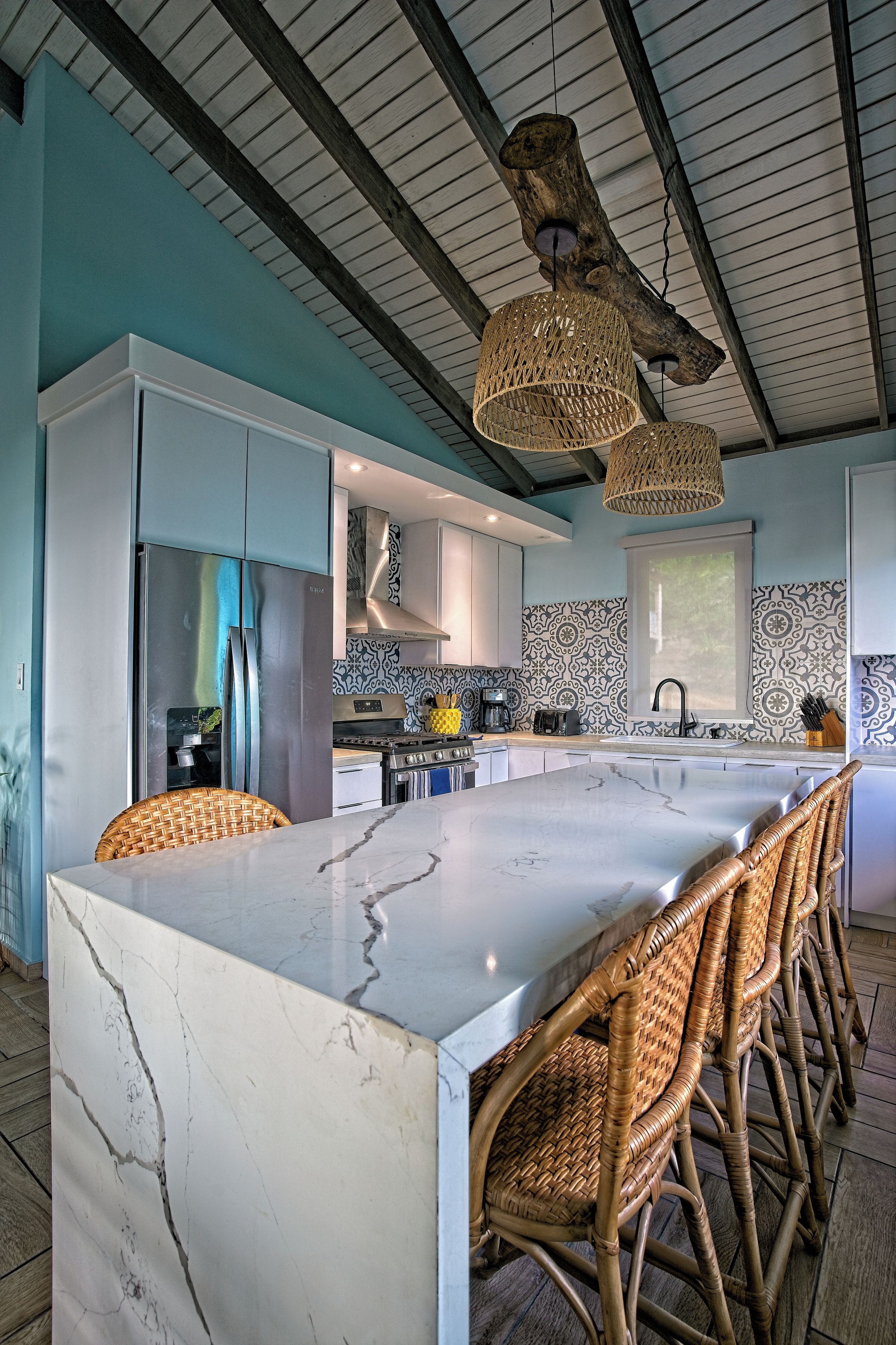Een moderne keuken met een groot eiland, rieten stoelen en een bijzonder plafondontwerp.