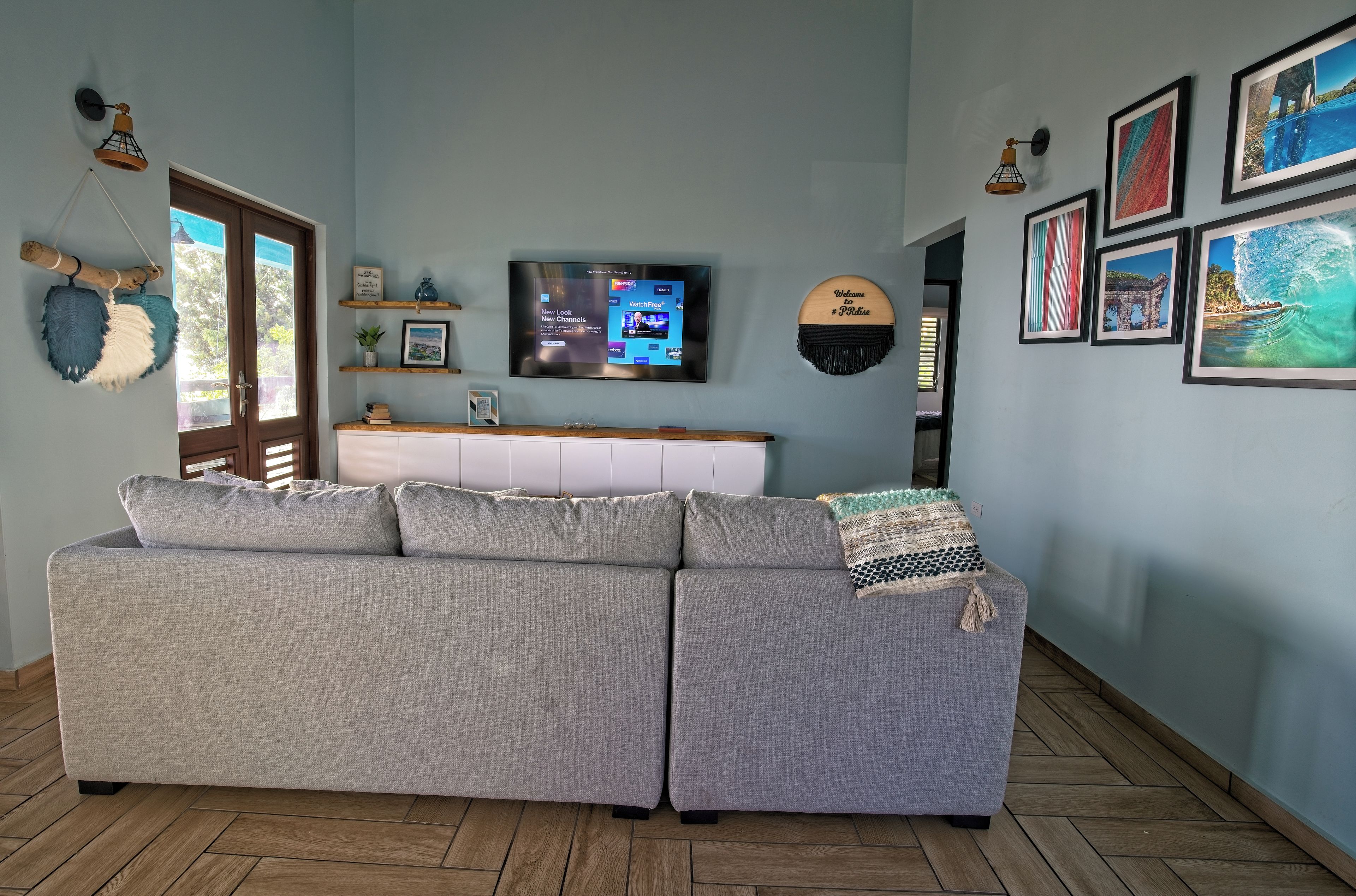 A living room with a grey sofa, a TV on the wall, and framed pictures.