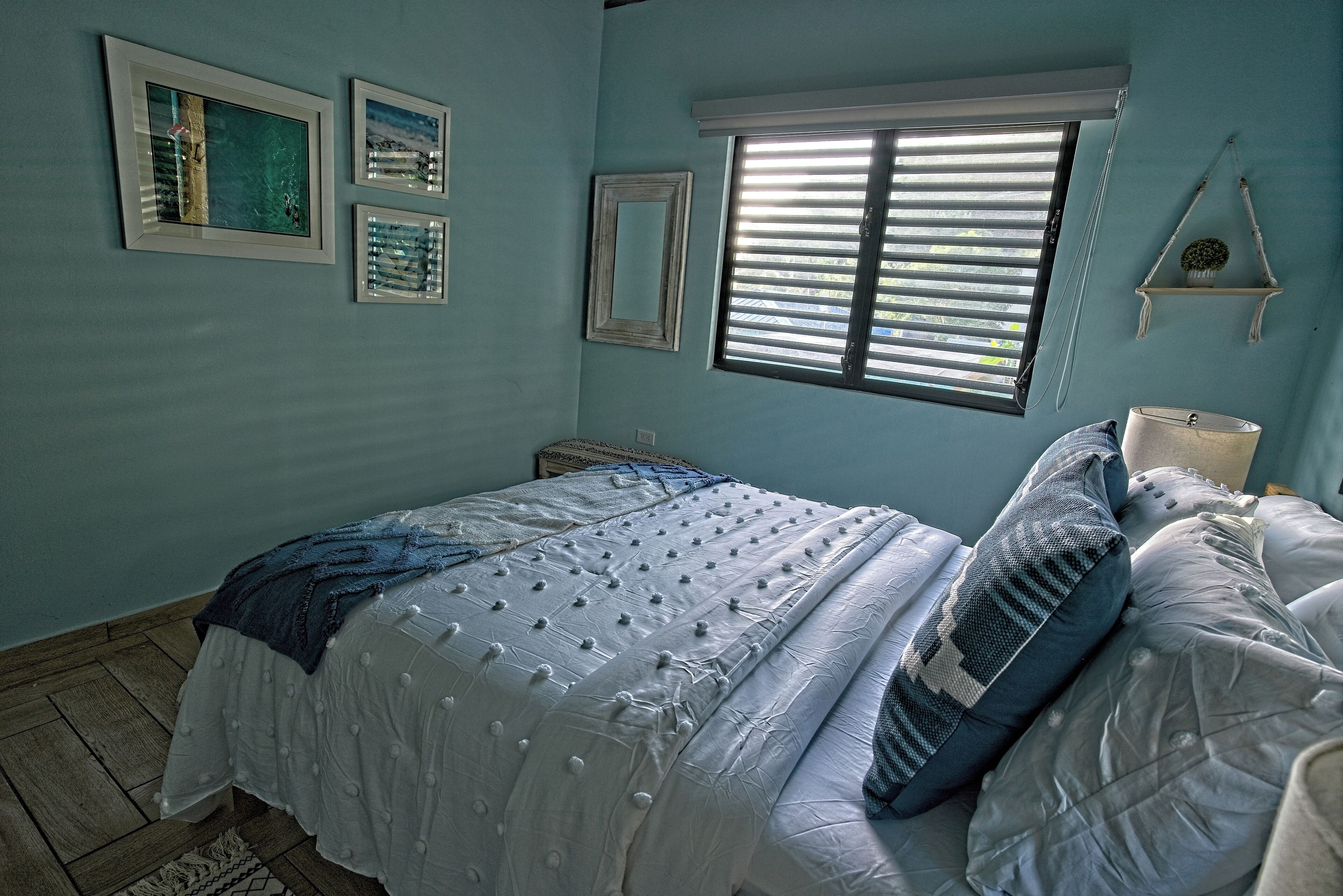 A bedroom with a bed, a window with blinds, and wall-mounted shelves.