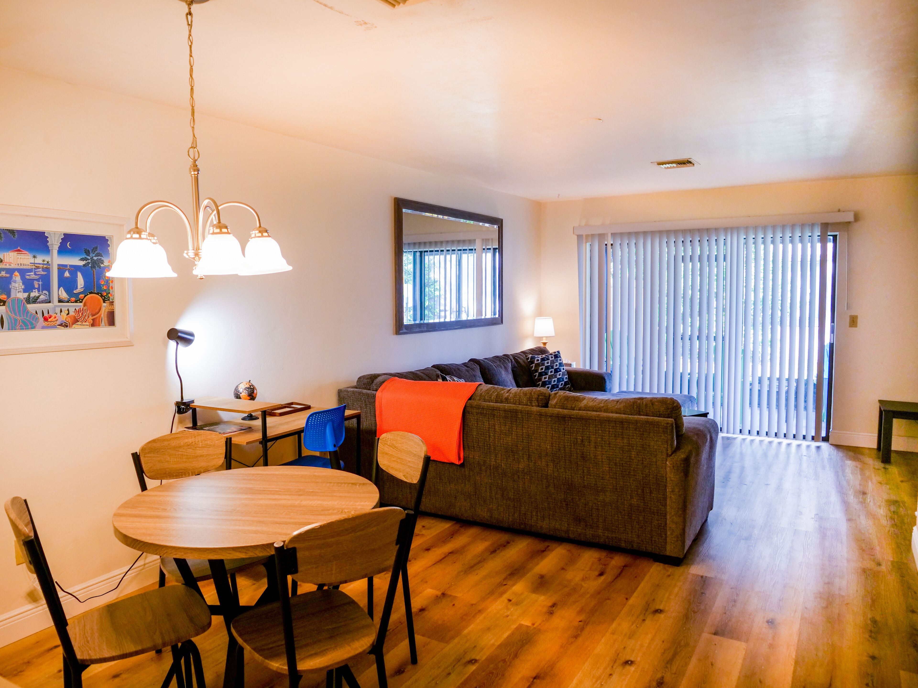 A living room with a wooden dining table and chairs, a sofa, and a large window with blinds.