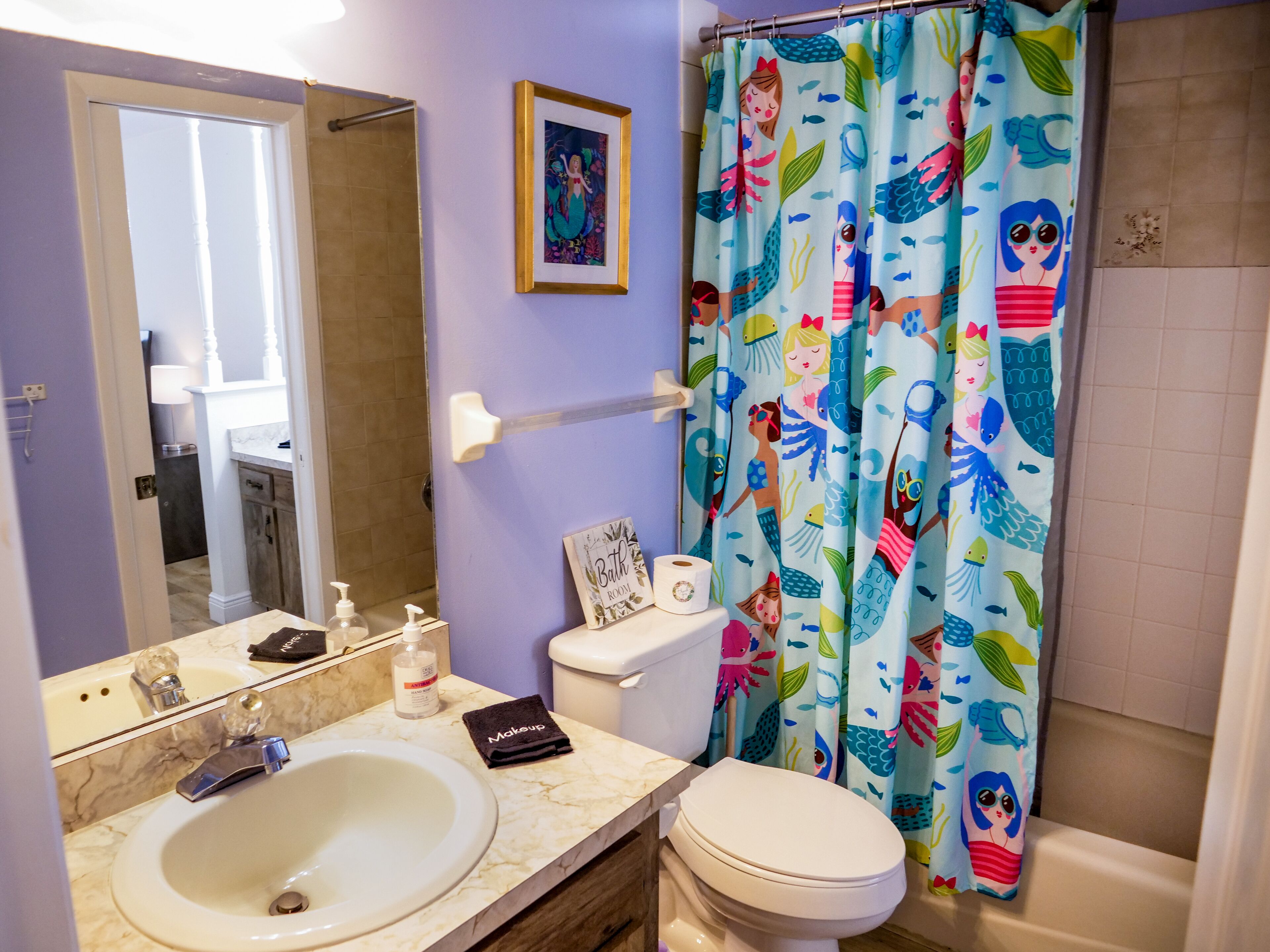 Ein Badezimmer mit Waschbecken, Toilette und Duschvorhang mit Meerjungfrau-Motiv.