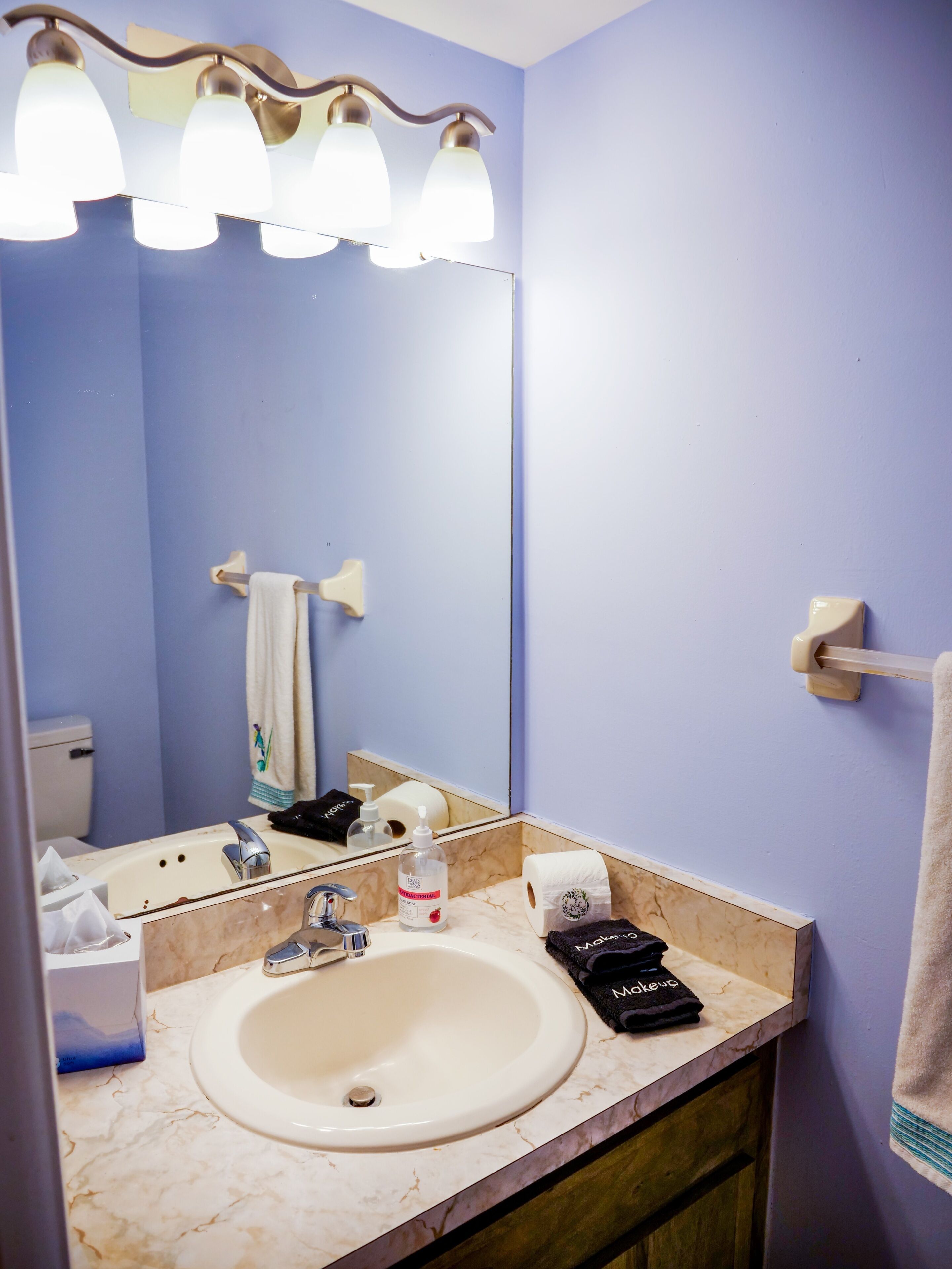 A bathroom with a sink, mirror, towel rack, and toiletries.