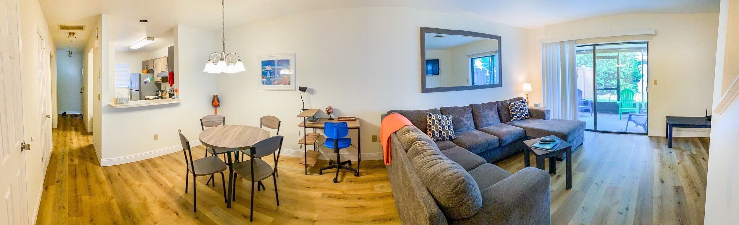 A modern living room with a sofa, a dining table with chairs, a kitchen area, and a large mirror.