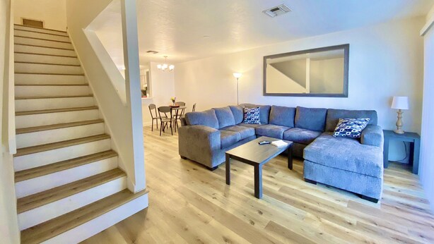 Un salon moderne avec un escalier en bois, un canapé d’angle, une table basse et un coin repas comprenant des chaises et une table.