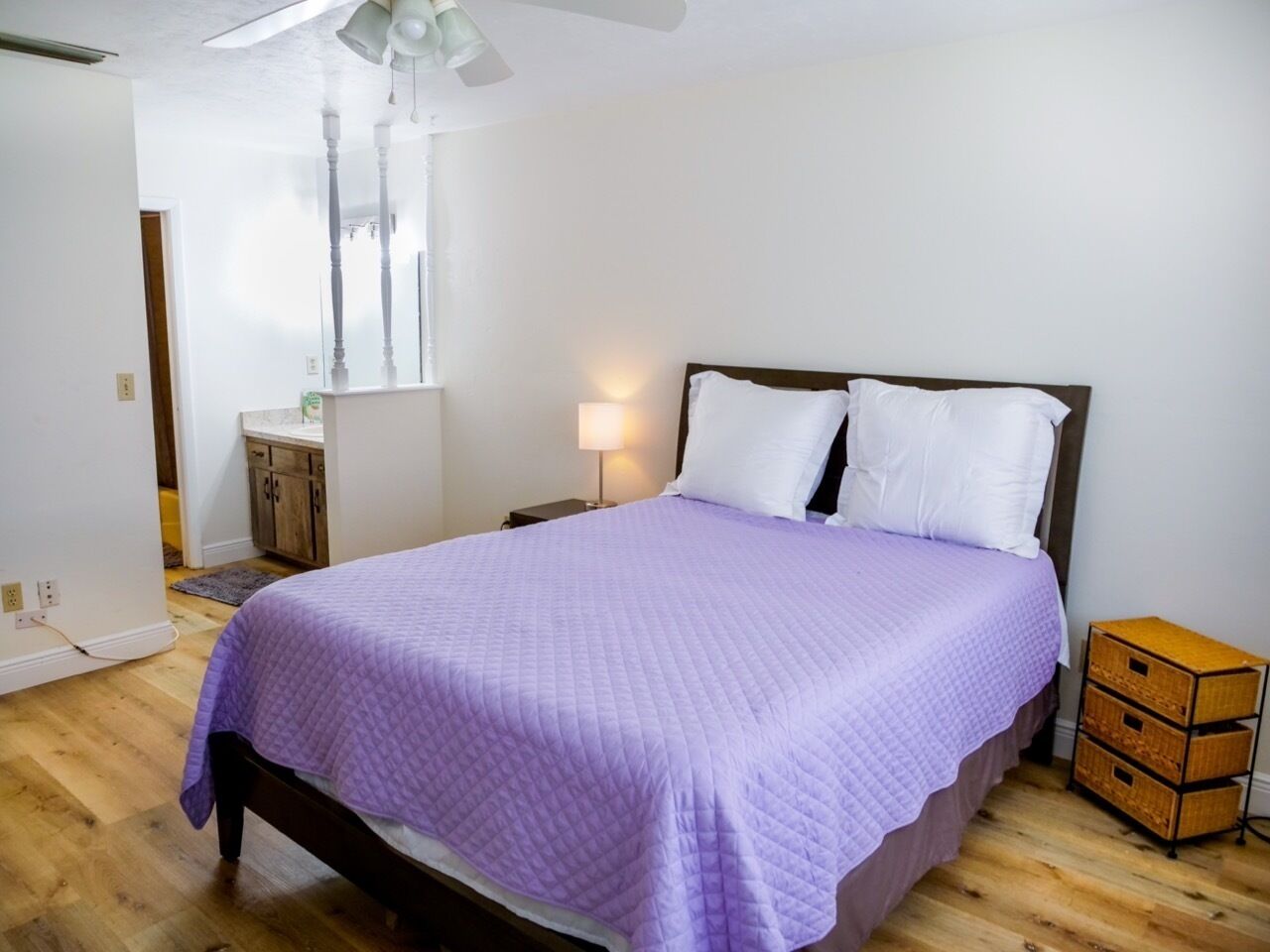 A bedroom with a bed, a nightstand, a lamp, and a wooden chest of drawers.