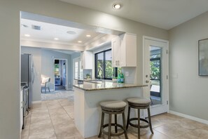 A modern kitchen with a central island, two barstools, and a view to the outdoors. - BEACHY PARADISE close to Siesta Key! (Sarasota)