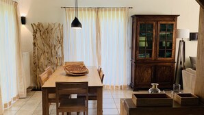 Een keuken met een houten tafel, stoelen, een hanglamp, een kast en een betegelde vloer.