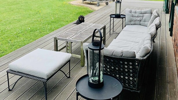 Een terras buiten met een bank, stoelen en een tafel.