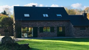 Een stenen herenhuis met twee verdiepingen, een donker dak, grote ramen en een gazon.