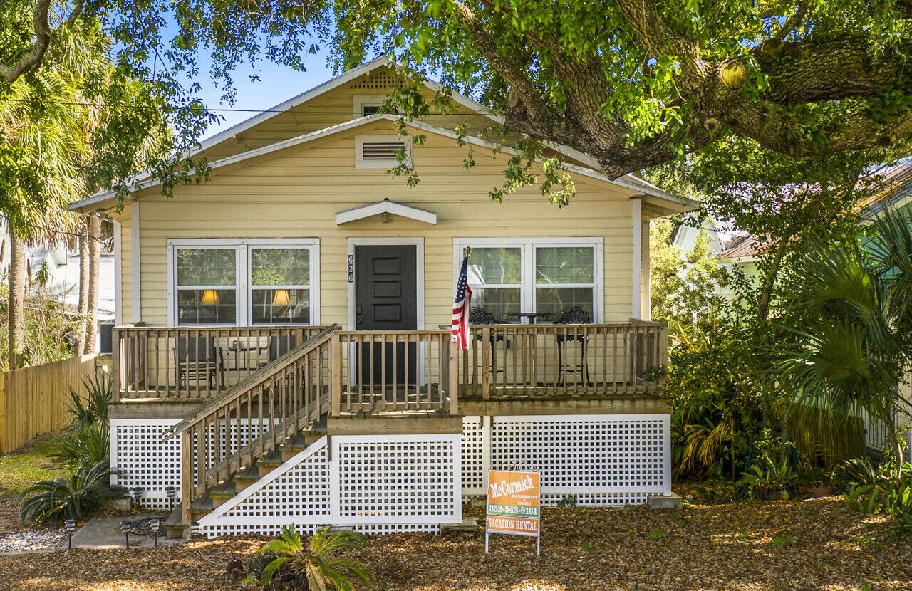 A two-story house with a front porch, a flag, and a sign indicating it is for vacation rental.
