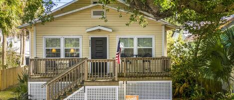 A two-story house with a front porch, a flag, and a sign indicating it is for vacation rental.