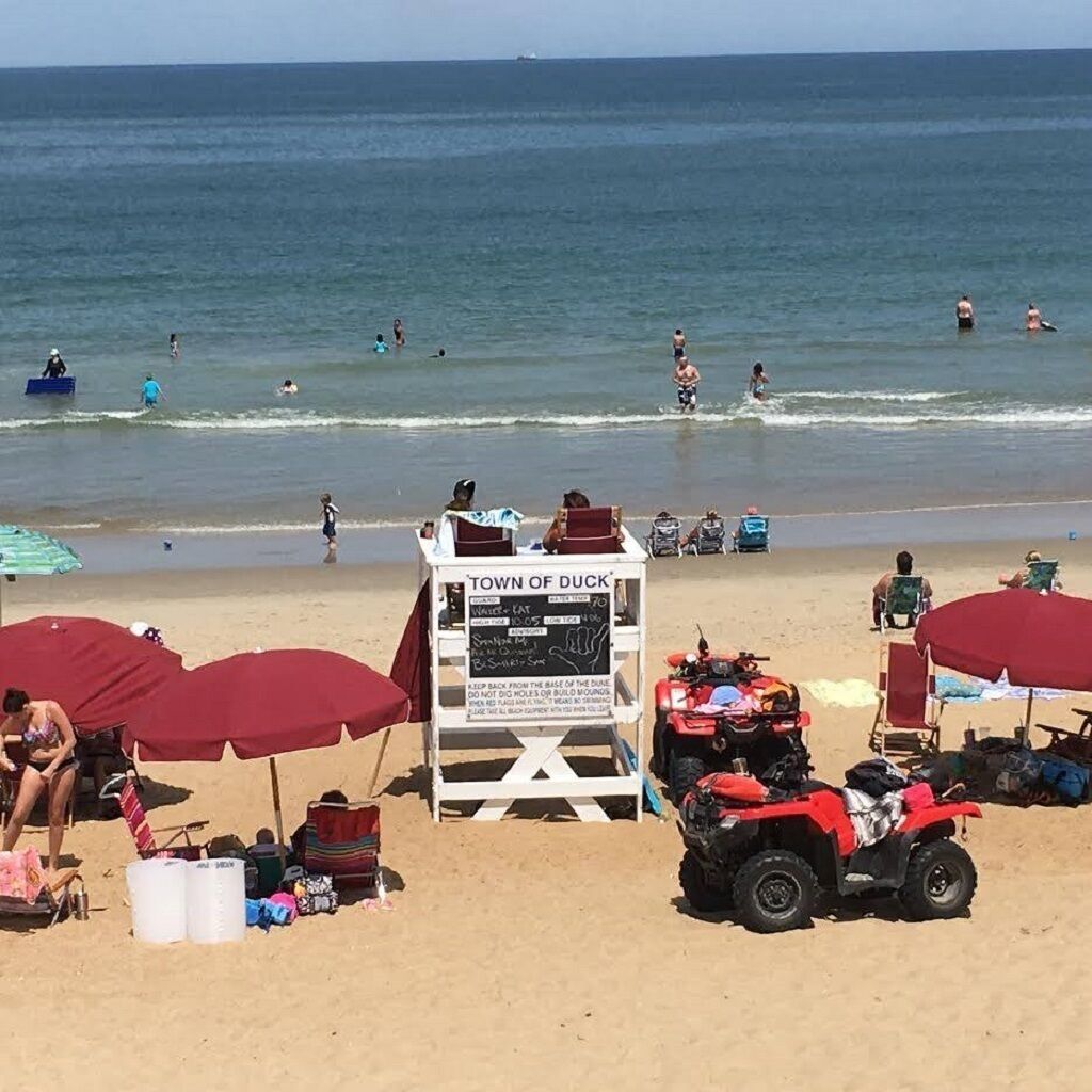 A beach with a lifeguard tower labeled "TOWN OF DUCK" and ATVs parked on the sand.