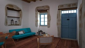 A room with a wooden floor, a blue door, a blue sofa, and a small table with a chair.