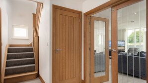 A staircase leading to a wooden door, a glass door leading to a living area with a sofa and a TV. - Hot Tub Haven, sleeps 8 in rural scenic Northumberland (Chatton)