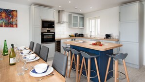 A modern kitchen with white cabinets, a central island with bar stools, and a dining area with a wooden table set for four. - Hot Tub Haven, sleeps 8 in rural scenic Northumberland (Chatton)