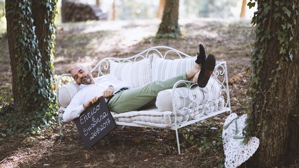A person lying on a white metal bench in a forested area with trees and foliage around. - La Castella (Villafranca d'Asti (AT))