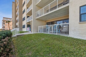 A multi-story residential building with balconies, a grassy lawn, and a clear sky.
