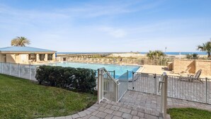 A swimming pool with a view of the beach, a covered area with lounge chairs, and a fenced patio area. - Direct Pool and Oceanfront Views | Ground Level Amelia By The Sea | Exclusive Access to the Pier (Fernandina Beach)