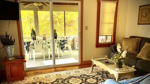Un salon comprenant un canapé, une table basse, un téléviseur et une porte-fenêtre coulissante donnant sur une terrasse extérieure avec une table et des chaises.