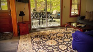 Un salon comprenant un canapé, une table basse, un téléviseur fixé au mur et une porte-fenêtre coulissante donnant sur une terrasse extérieure avec une table et des chaises.