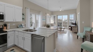 Une cuisine spacieuse avec un grand îlot central, un coin repas avec une table et des chaises, et un salon avec un canapé et un téléviseur.