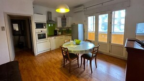 Cocina compacta con armarios blancos, microondas, horno y campana extractora verde. Hay una mesa de comedor con cuatro sillas y una lámpara colgante.