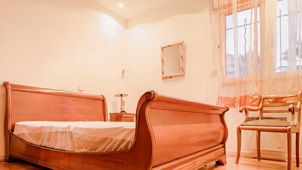 Un dormitorio con una cama de madera, una mesita de noche, una silla y una ventana con cortinas.