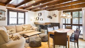 Un salon chaleureux avec un canapé, une table basse, des poufs et une table à manger avec des chaises. On y trouve également une cheminée, un miroir fixé au mur et un luminaire suspendu.