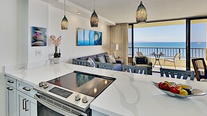 A modern kitchen with a central island, an oven, and a dining area with a view of the sea. - Where the Pacific Stretches Forever Kihei Remodeled Oceanfront Condo Pool (Kihei)