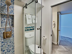 A modern bathroom with a glass-enclosed shower, white fixtures, and a mosaic tile backsplash.