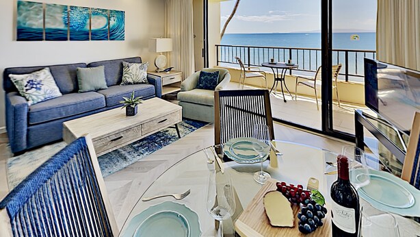 A modern living room with a sofa, coffee table, and dining area with a view of the sea. - Where the Pacific Stretches Forever Kihei Remodeled Oceanfront Condo Pool (Kihei)